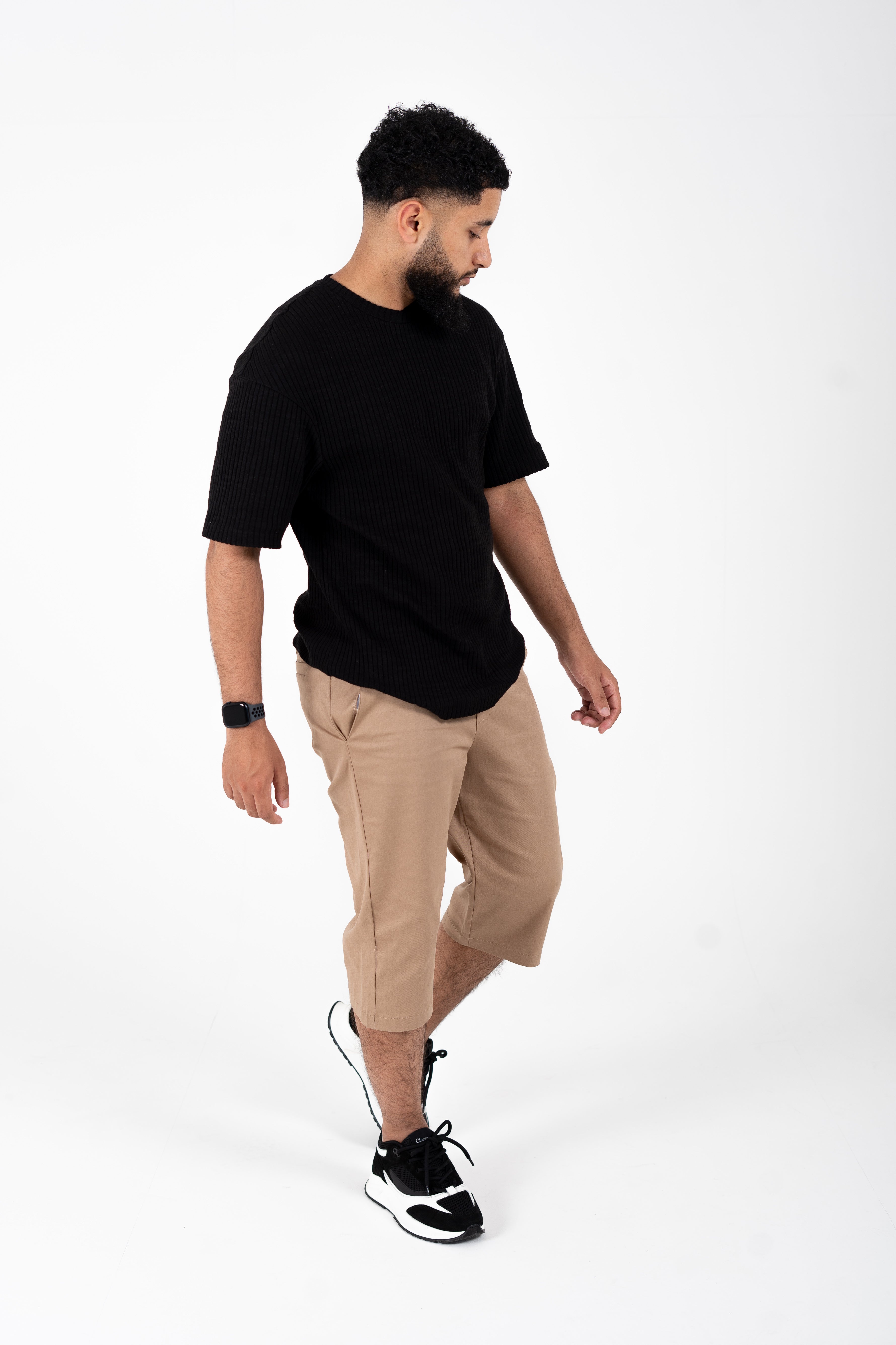 Full-body walking shot wearing sand chino shorts with black tee and sneakers