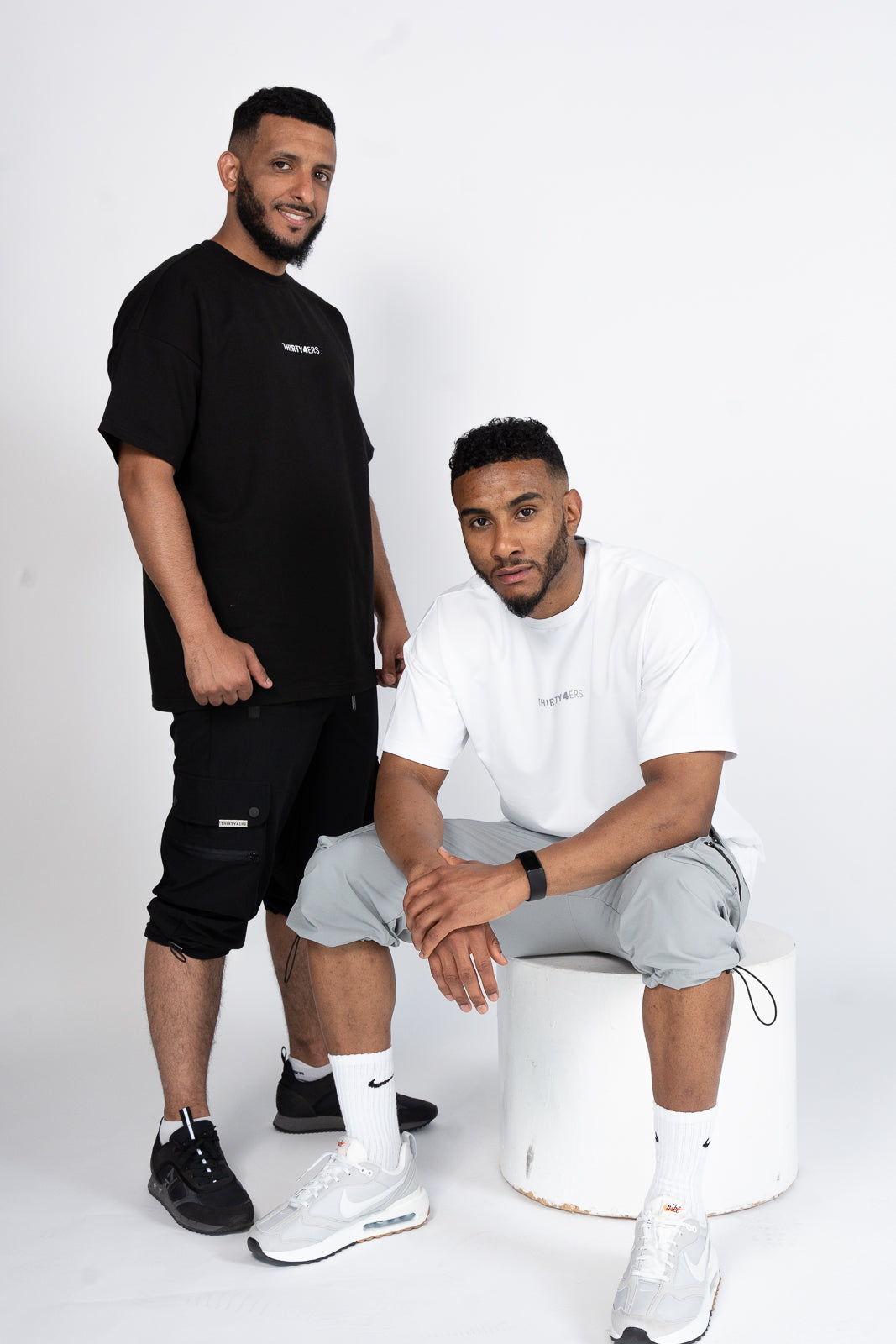 Two men wearing black and white modest gym outfits featuring 34ERS® cargo shorts