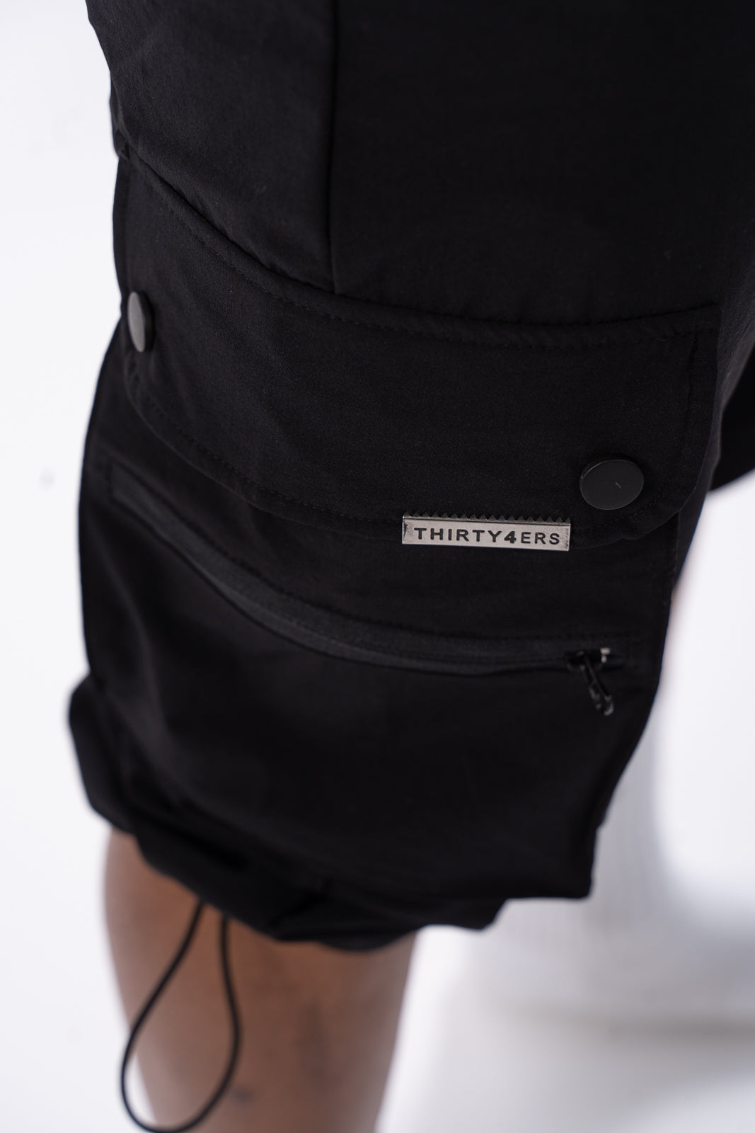 Zoomed view of embossed 34ERS® metal brand plate on black cargo pants