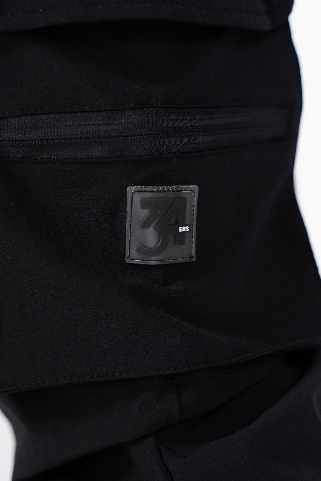 Back close-up of 34ERS® men’s 3/4 cargo shorts showing metal branding plate and snap pocket flap