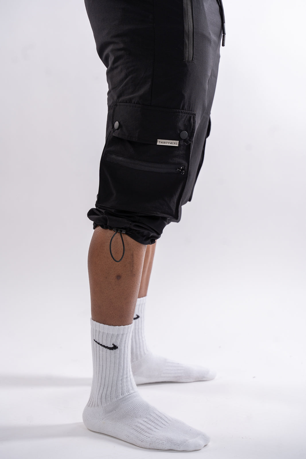 Side view of black modest men’s cargo shorts covering knees with adjustable bungee cords